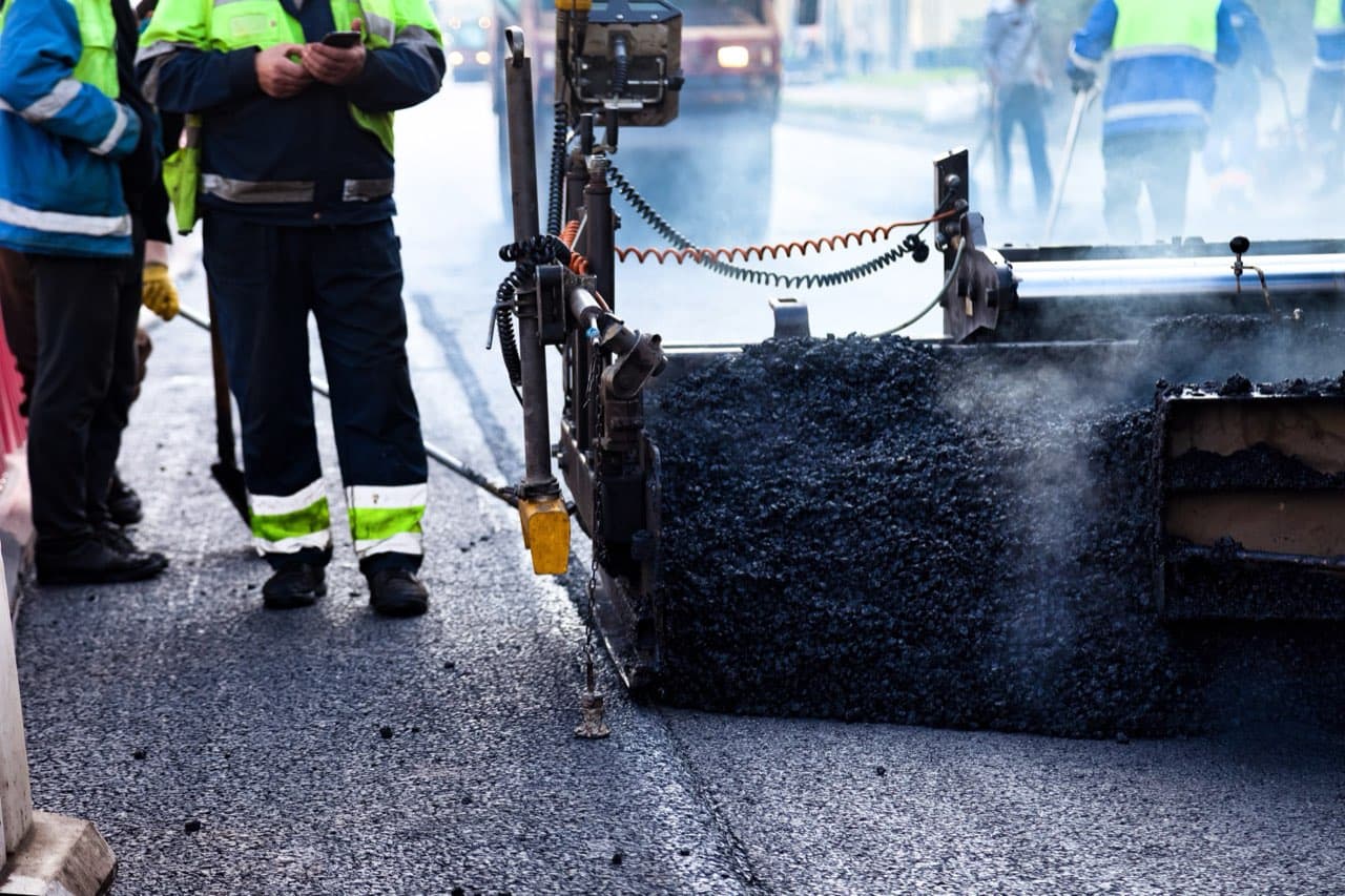 Construction crew paving a city street with a yellow paver machine